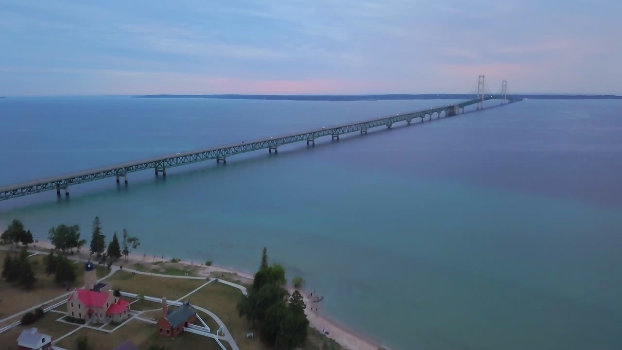 cinematográfico drone aéreo faro del puente mackinaw michigan puesta de sol púrpura rosa impresionante paisaje de los grandes lagos a mediados del verano en el norte de petoskey puerto manantiales coches pacíficos cruzan el puente hacia adelante pan up