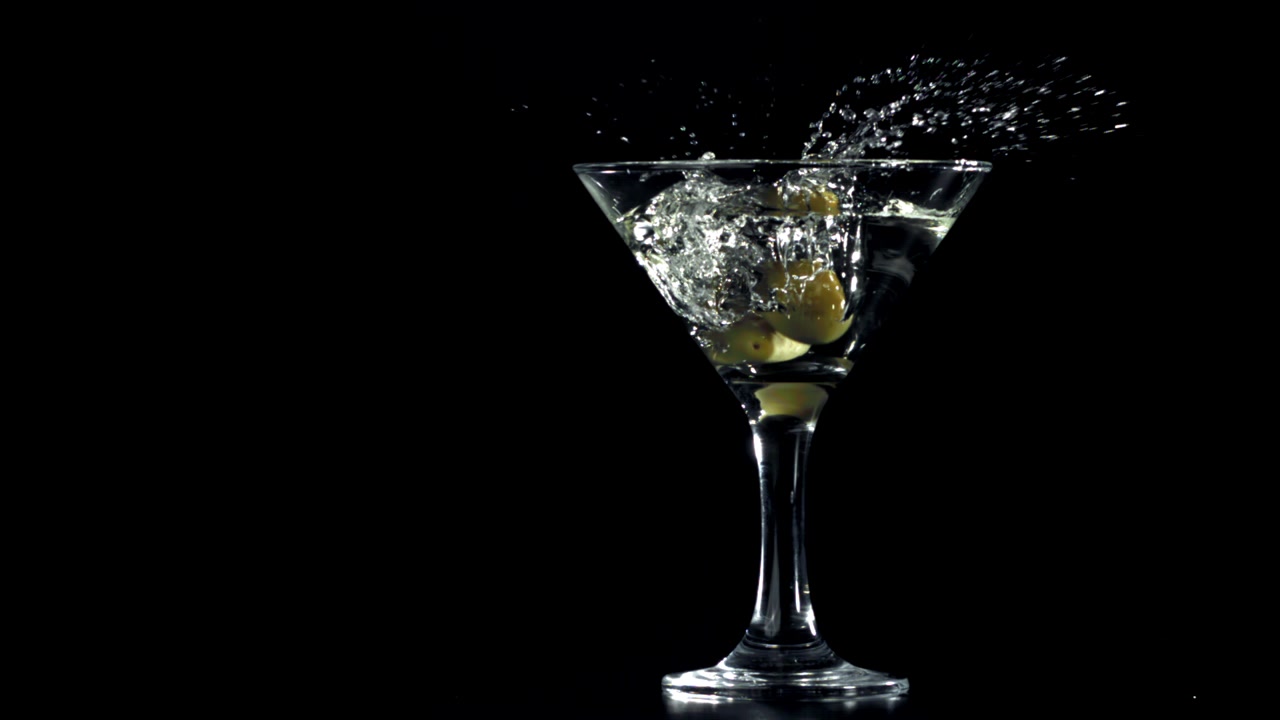 Oliva che cade in un bicchiere da Martini con schizzi al rallentatore