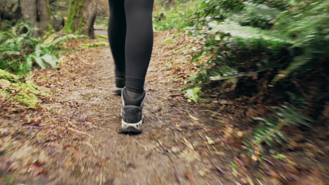 Uma Jovem Mulher Vestindo uma Jaqueta Amarela Brilhante Caminha por uma Floresta Verde Musgosa, Plano Detalhe em Movimento de Suas Botas