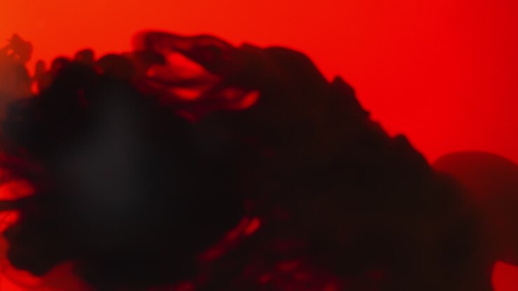 Red And Black Paint Or Dye Dropped Into Water Against White Background To Create Swirling Colourful Smoke Background