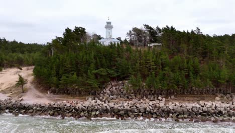 Faro-Aéreo-Blanco-En-Una-Colina-Con-Vistas-A-Un-Cuerpo-De-Agua,-Rodeado-De-árboles-Verdes,-Día-Nublado,-Camión-Derecho,-Faro-De-Uzava