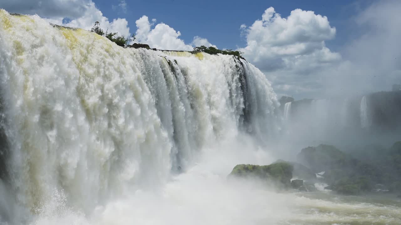 hermosos cielos azules en condiciones climáticas soleadas, increíbles cascadas enormes que se estrellan en grandes piscinas de agua rocosa, vistas coloridas y brillantes en las cataratas de iguazu, brasil, américa del sur