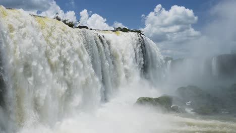 beautiful blue skies in sunny weather conditions, amazing huge waterfalls crashing into large rocky water pools, bright colourful views in iguazu falls, brazil, south america