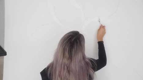 back view of a person spreading white acrylic paint on canvas using a palette knife