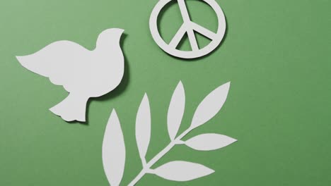 Close-up-of-white-dove-with-peace-sign-and-leaf-and-copy-space-on-green-background