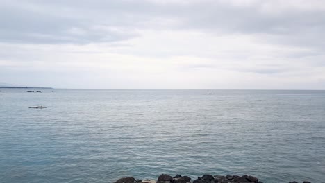 drone view rising from black lava rocks viewing blue ocean of hawaii on overcast day