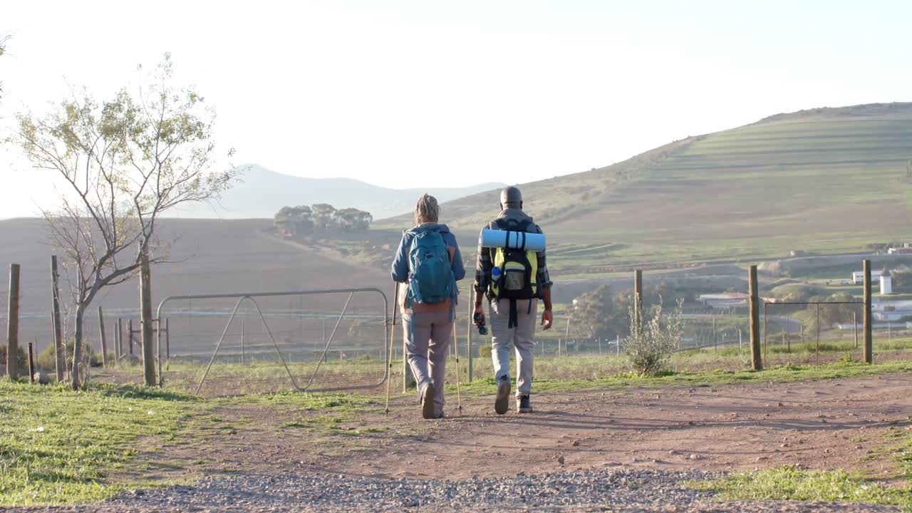 pareja de ancianos afroamericanos con mochilas caminando en la naturaleza soleada, cámara lenta