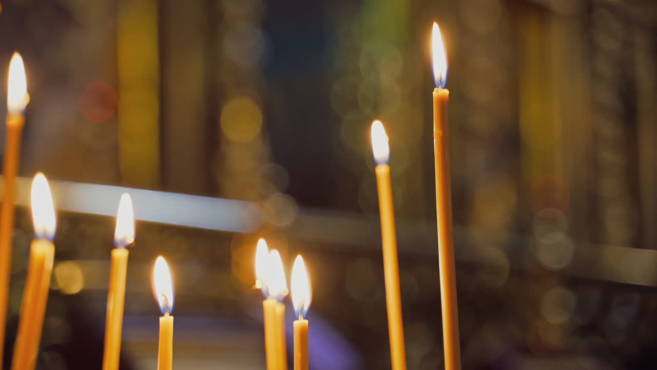 Beeswax candles are glowing on the blurred background. Church candles burning in the night temple. Candles are lit for prayer intentions.