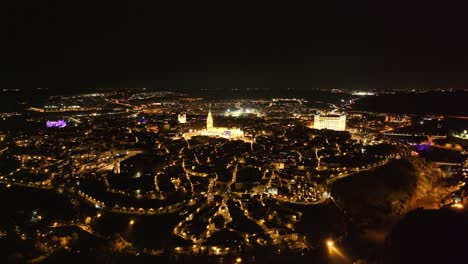 drone descent flight filming the spectacular city of toledo at night, we see the cathedral and the alcazar with spectacular lighting and the rest of the street lights create that nocturnal magic