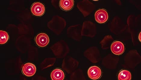 overhead shot of romantic lit red candles revolving on background covered in rose petals with copy space