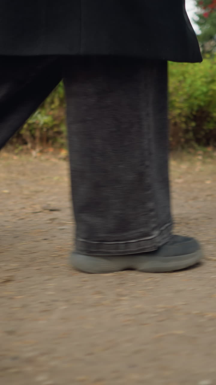 vista lateral dinámica de las piernas de una persona en vaqueros negros y zapatos de lona, capturando la esencia de un paseo de otoño a través de un jardín con follaje vívido y tonos terrenales