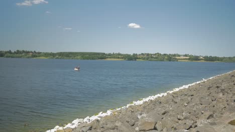 sunny shot of a reservoir, boat sailing in the distance alongside a rocky border with sand shot on a gh4