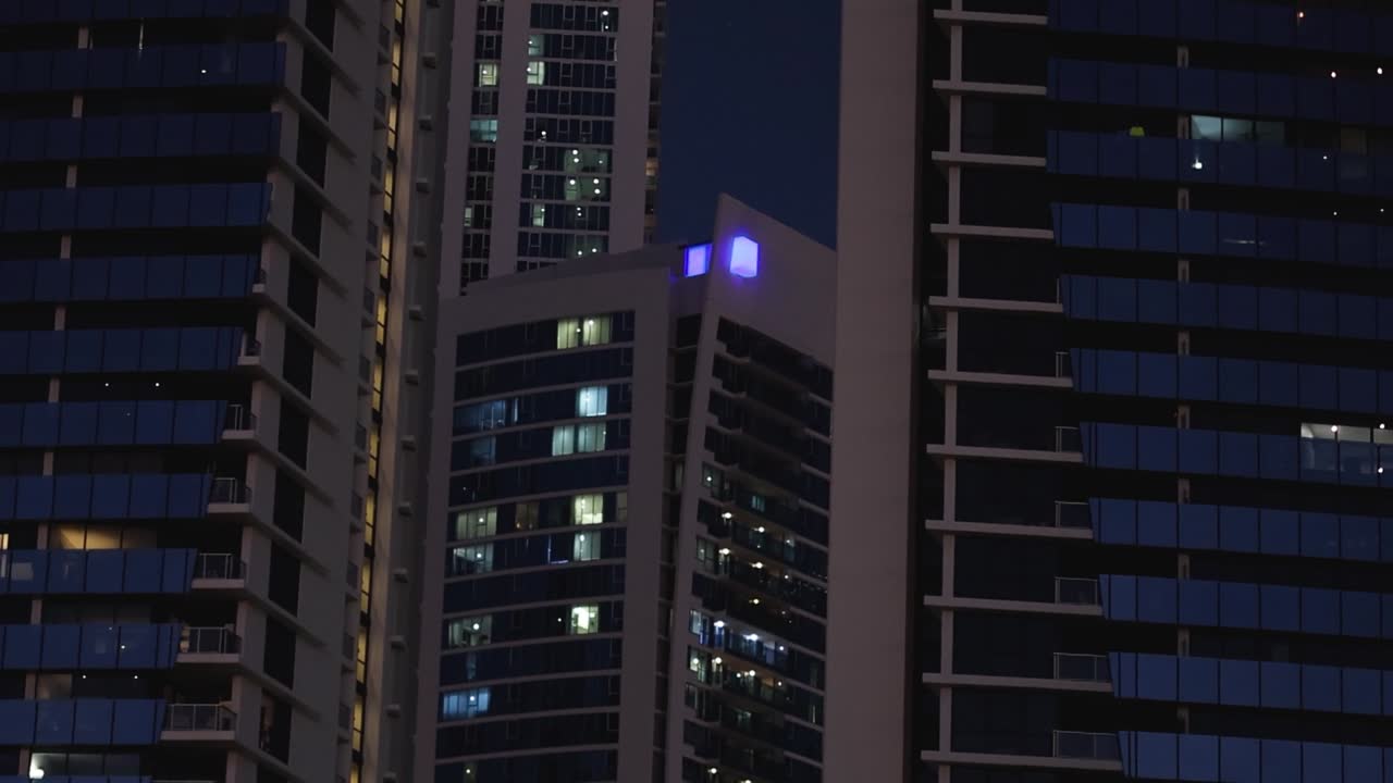 Detailed view of a skyscraper's lit windows and blue lights against the night sky.