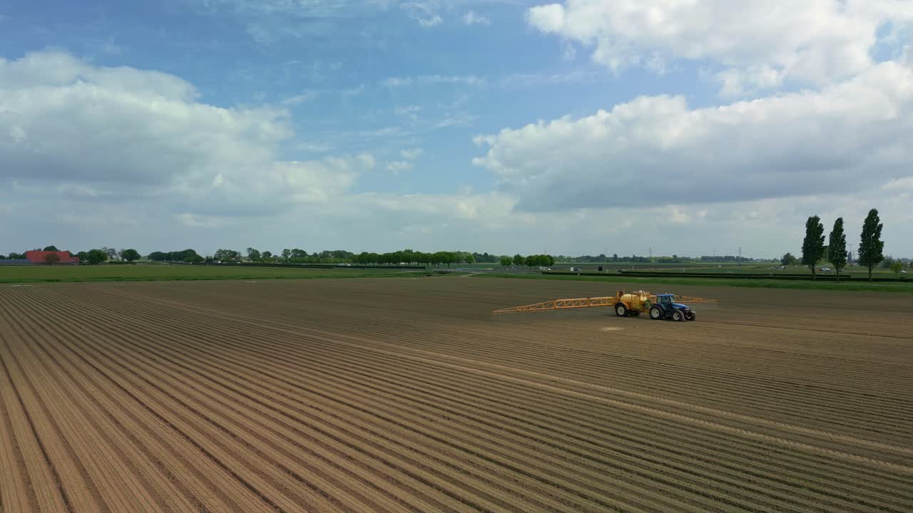 A tractor sprays the field with crop protection products on a partly cloudy day