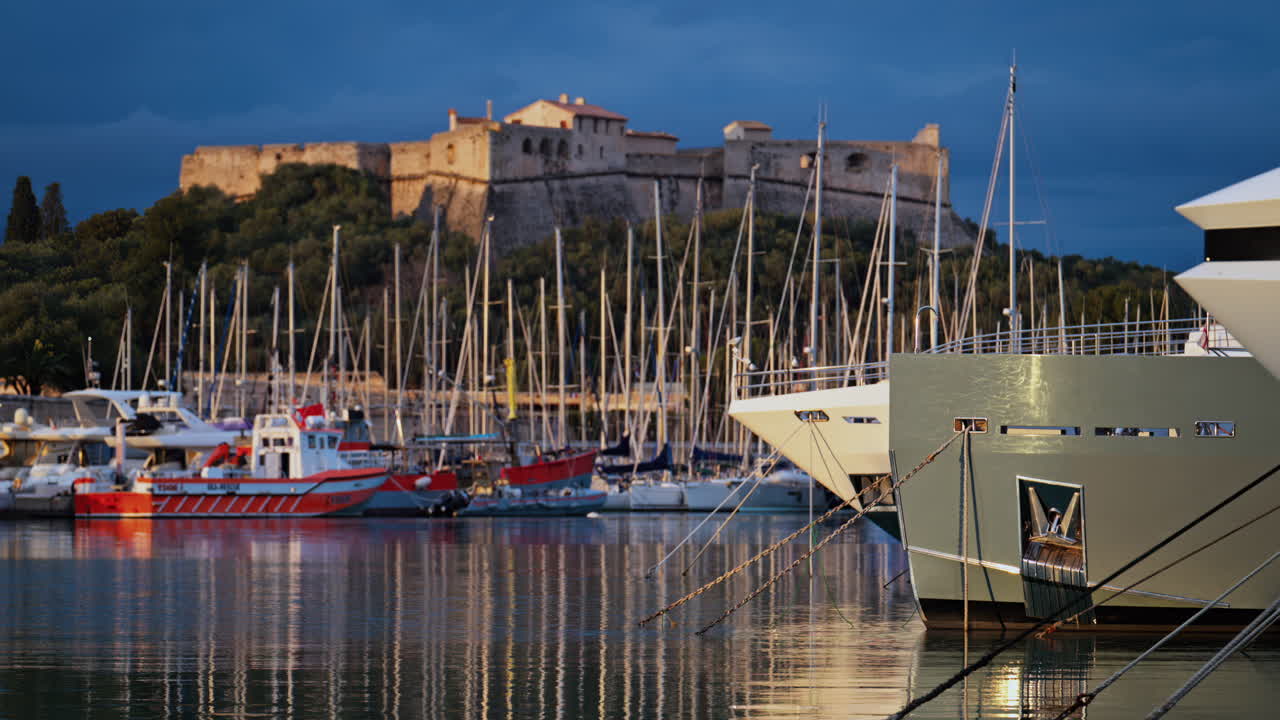 Båtar som ligger i hamnen i Port Vauban med Fort Carre i bakgrunden vid solnedgången i Antibes, Frankrike