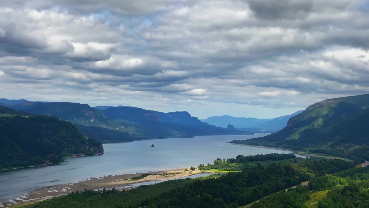 Pemandangan panorama Ngarai Sungai Columbia dengan sungai berkelok-kelok, bukit-bukit tertutup hutan, dan pegunungan berlapis di bawah langit berawan, pemandangan udara.