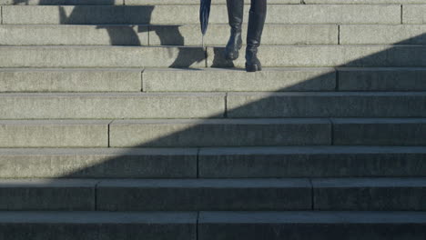 woman in black boots walking down stone steps casting a shadow