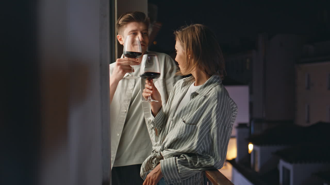 Couple talking night date on balcony. Relaxed lovers celebrate clinking glasses