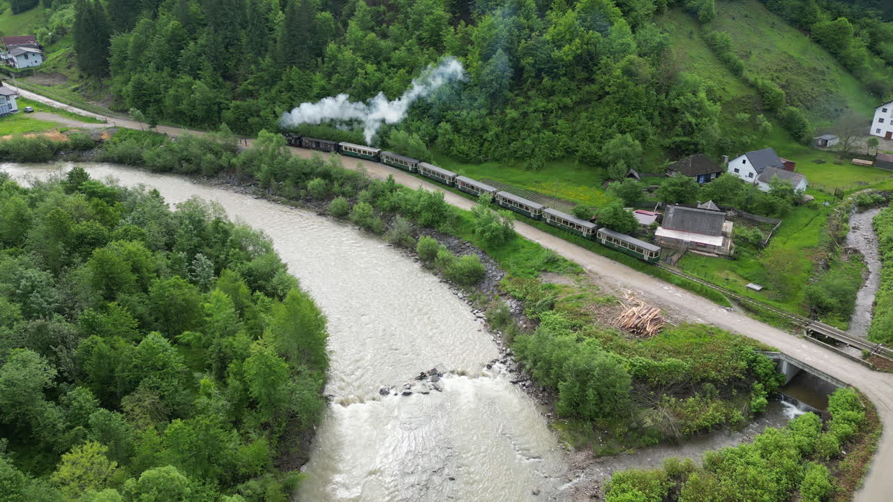 Aerial view: Mocanita steam train traveling along the Vaser river in Maramures Mountains, Romania