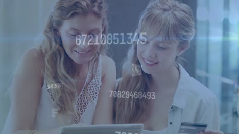 Animation-of-changing-numbers-over-caucasian-female-friends-shopping-on-laptop-using-credit-card