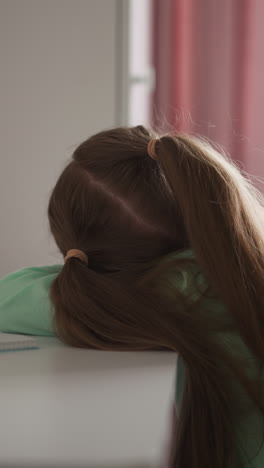 exhausted little girl with long loose hair lies on desk sitting in children room. upset student do not want to do homework at table after school classes