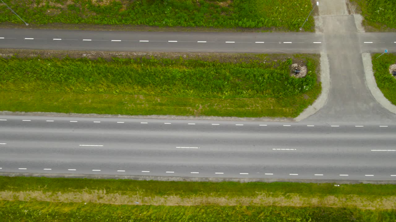 Top down aerial drone footage gliding and flying over sideways over a rural countryside highway where a cyclist and pedestrian road is separated from it by grassy area. Cloudy summer day, vehicles