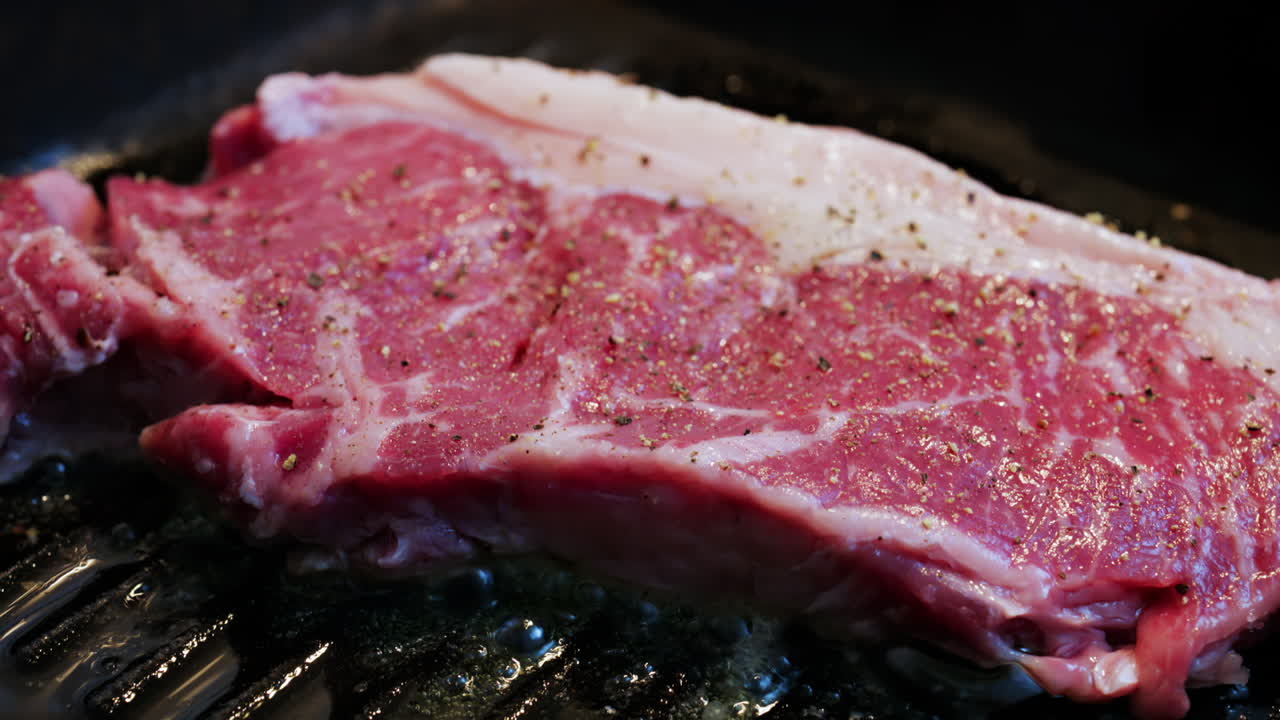 Fresh raw steak sizzling on a hot grill pan with visible seasoning and cooking oil