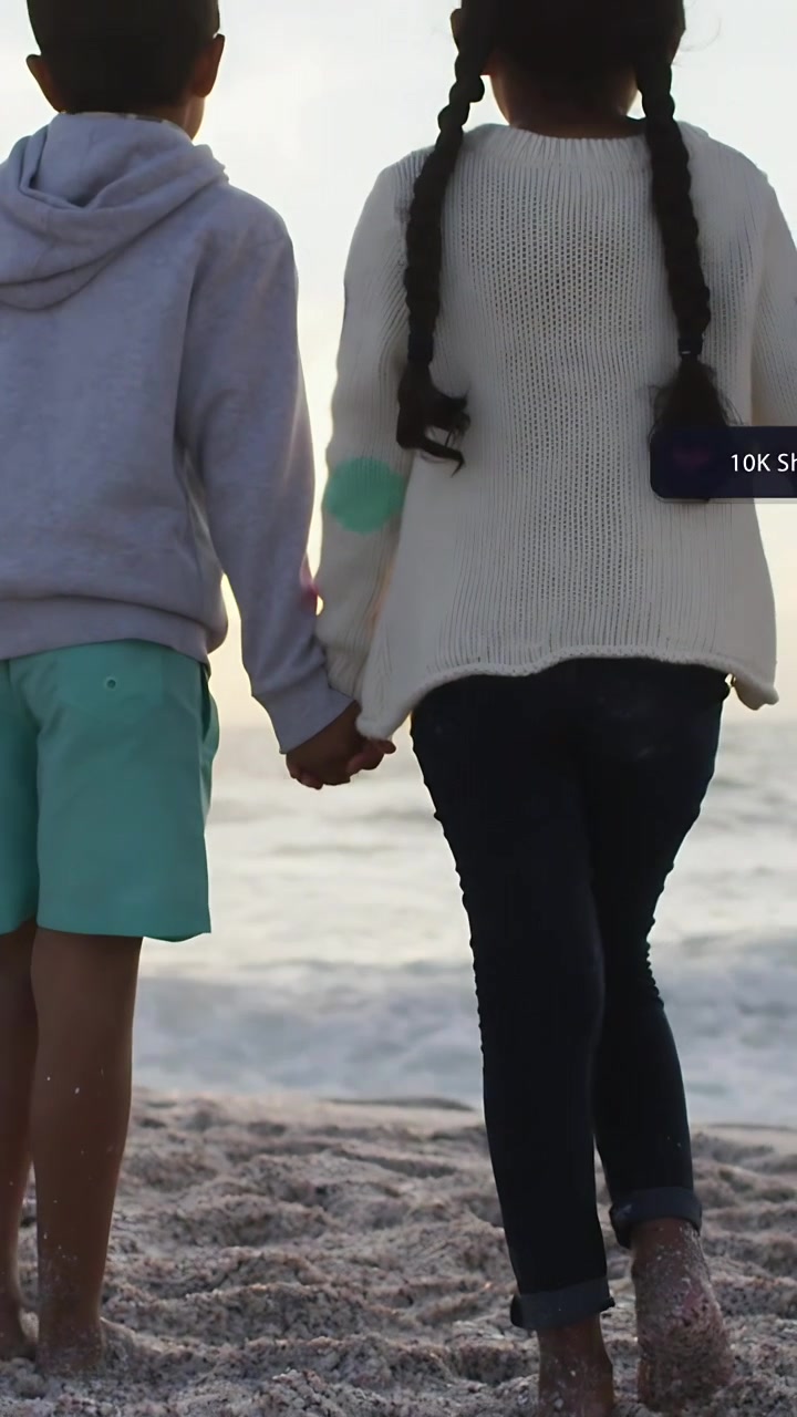 Vertical video: Boy and girl walking hand-in-hand toward ocean, surrounding animated social metrics