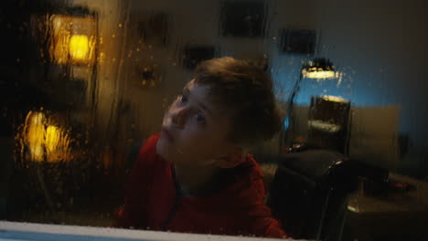 boy in wheelchair looking out rainy window