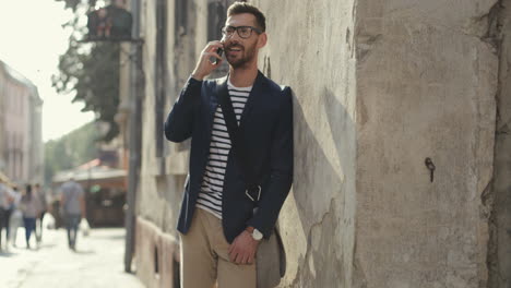 stylish man leaning against the wall in the old town street and talking on the mobile phone