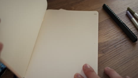 opening black work notebook under bright sunlight on top of cozy wooden desk with pens