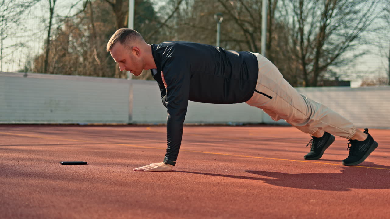 Un giovane in tuta da ginnastica e maglia sportiva fa sport su un campo da basket. Un uomo dal corpo atletico si allena all'aperto.