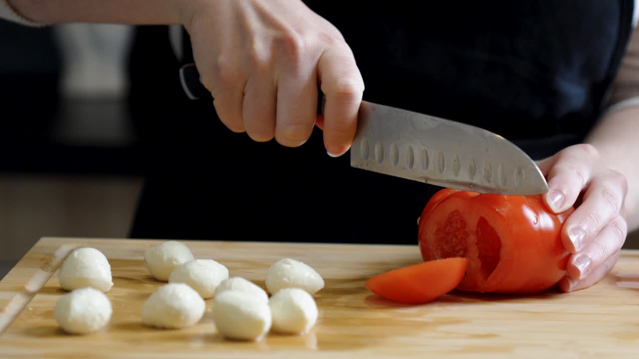 slowmotion of a hand slicing a fresh large red tomato ready to be used in a dish
