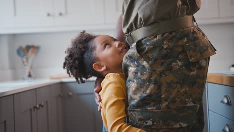 close up of daughter hugging legs of army father in uniform home on leave in family kitchen