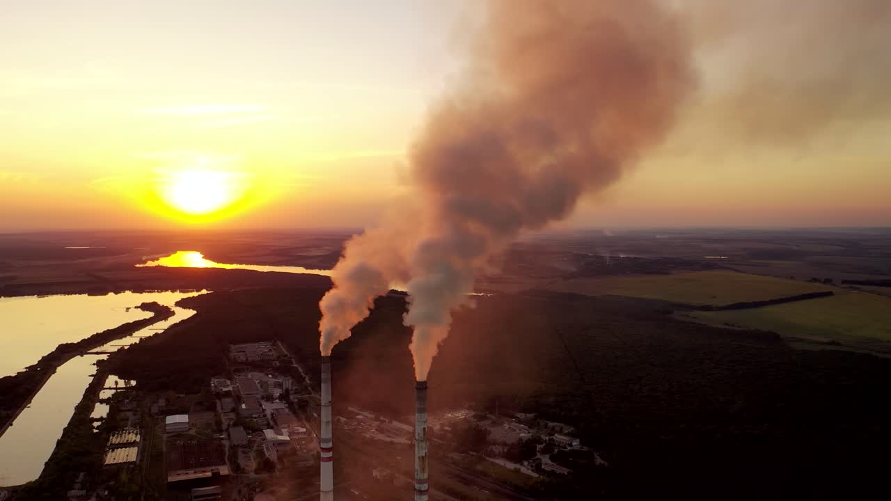 Metallurgical plant at sunset. Smoke coming out of factory pipes on the natural background. Aerial view. Camera moves back.