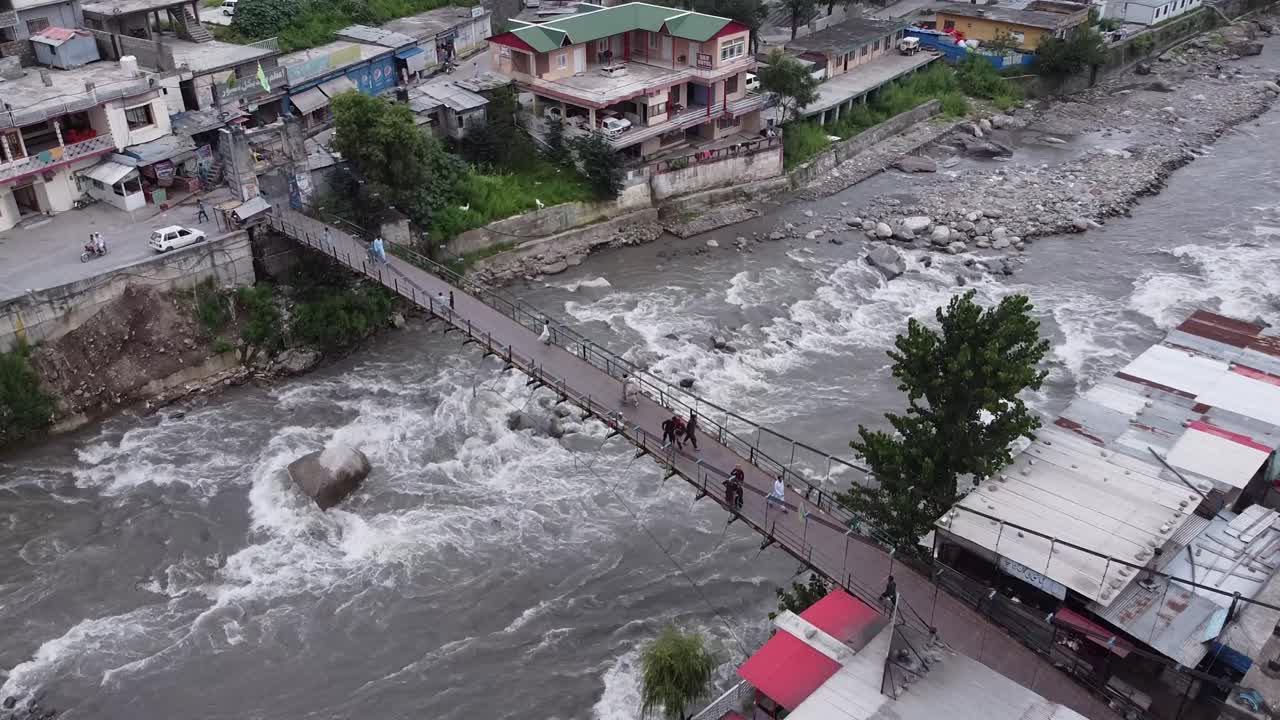 Aerial View of People Walking on a Bridge over a Fast-Flowing River in a Mountain Town