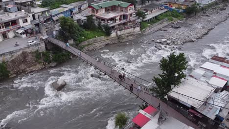 aerial view of people walking on a bridge over a fast-flowing river in a mountain town