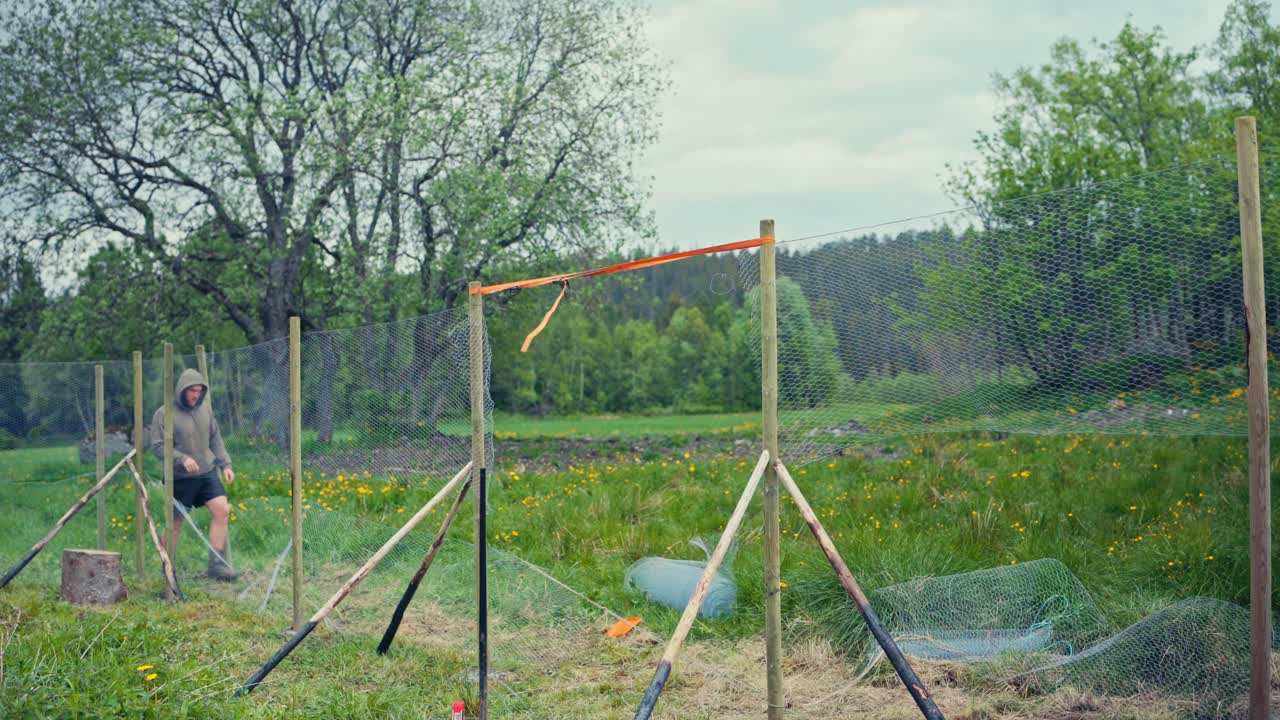 Man Building Fence With Metal Wire Mesh - Wide Shot