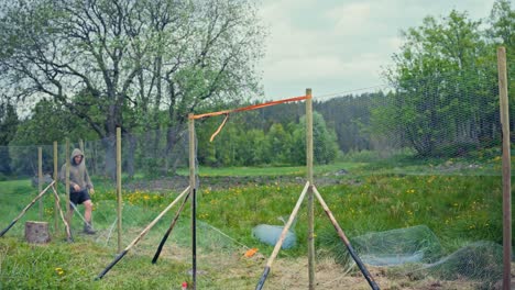 man building fence with metal wire mesh - wide shot