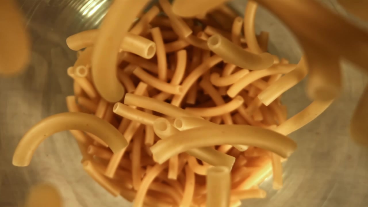 Maccheroni secchi che cadono in una ciotola di metallo al rallentatore