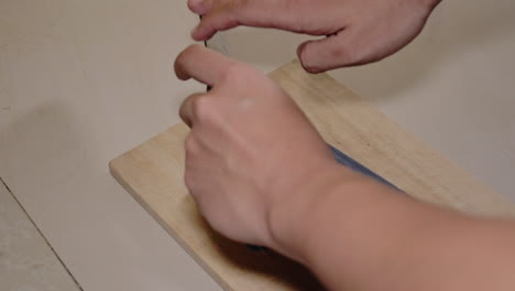 hand of man sharpening knife with whetstone sharpener over the wooden chopping board