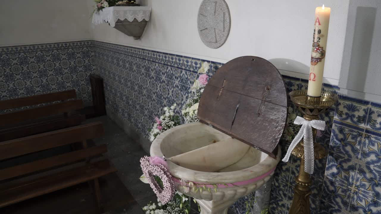 Baptismal font with open wooden lid candle floral decoration and tile walls