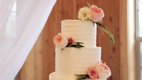 close up of round, layered wedding cake on a table decorated with white textured frosting and pink flowers 1080p 60fps