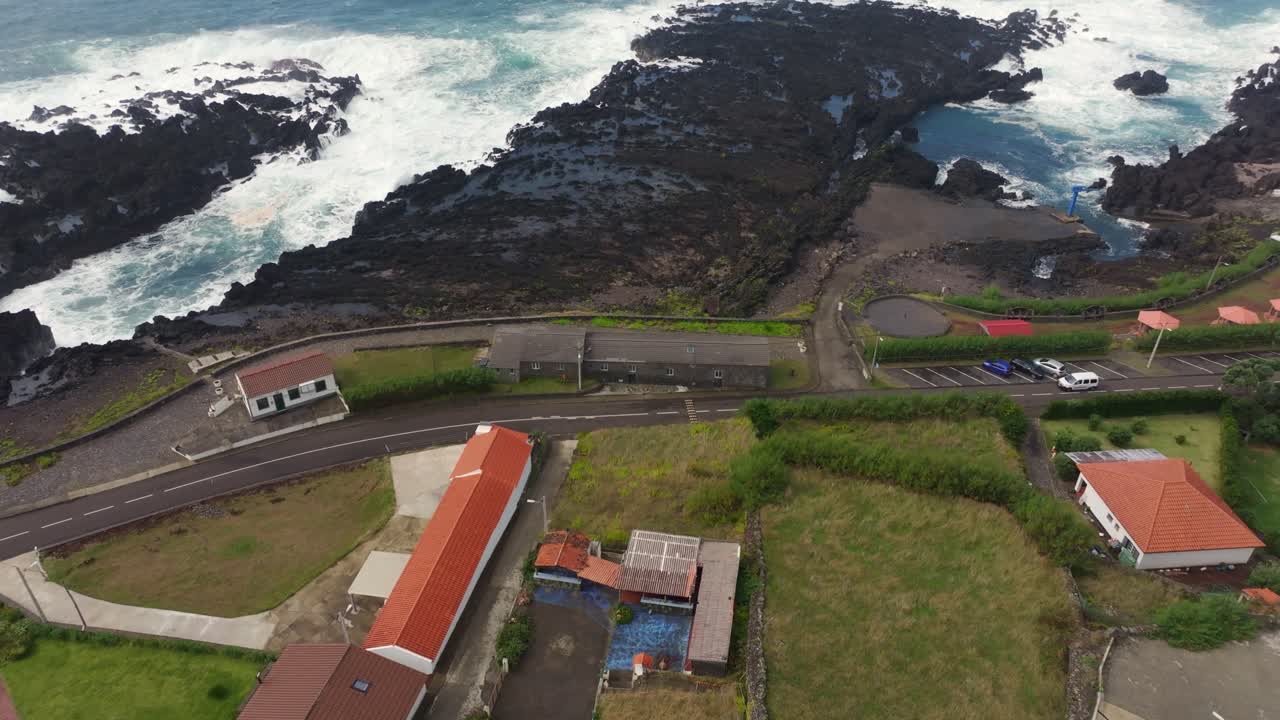 Vista aerea del villaggio di Faja Grande con case, rocce e potenti onde dell'Atlantico settentrionale che si infrangono lungo la costa di Flores.