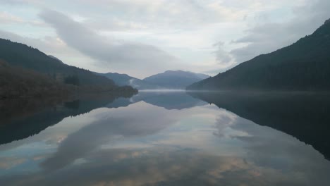 drone flight over mirror-like water with mountain scenery