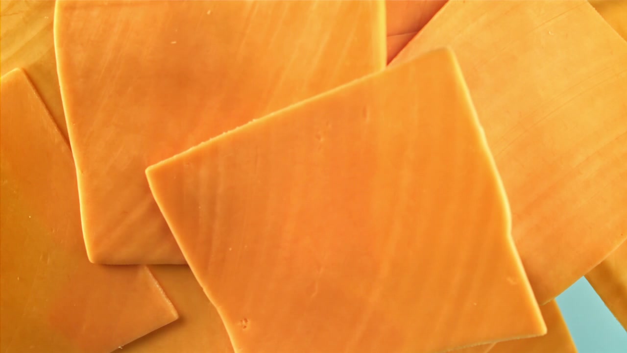 Primo piano di fette di formaggio Cheddar impilate su sfondo blu.