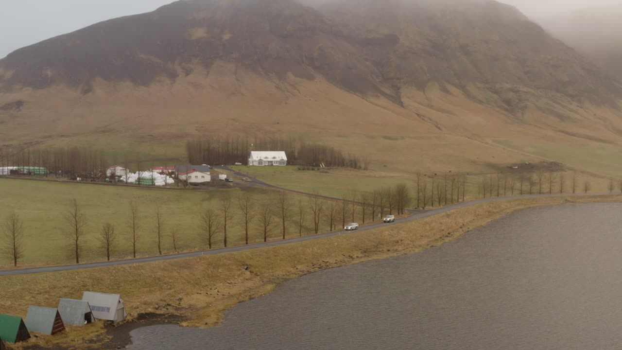 Mutkitteleva rannikkotie, joka kulkee pienen maatilan ohi sumuisten vuorten alla Hvalfjörðurissa, Islannissa