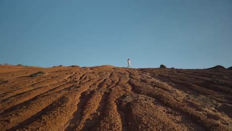 mujer distante caminando sobre la cresta del paisaje en forma de erosión en un día soleado
