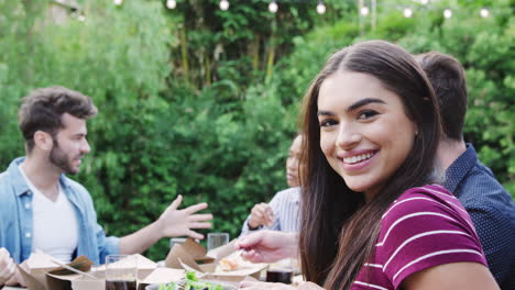 portrait of woman with friends at home sitting at table enjoying food at summer garden party