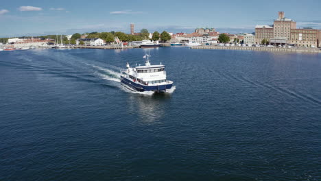 Aerial-drone-shot-of-transport-passenger-ferry-ship-boat-leaving-a-rural-urban-small-city-port-in-the-morning-taking-a-group-of-tourist-over-the-sea-to-an-island-for-vacation-during-sunny-summer